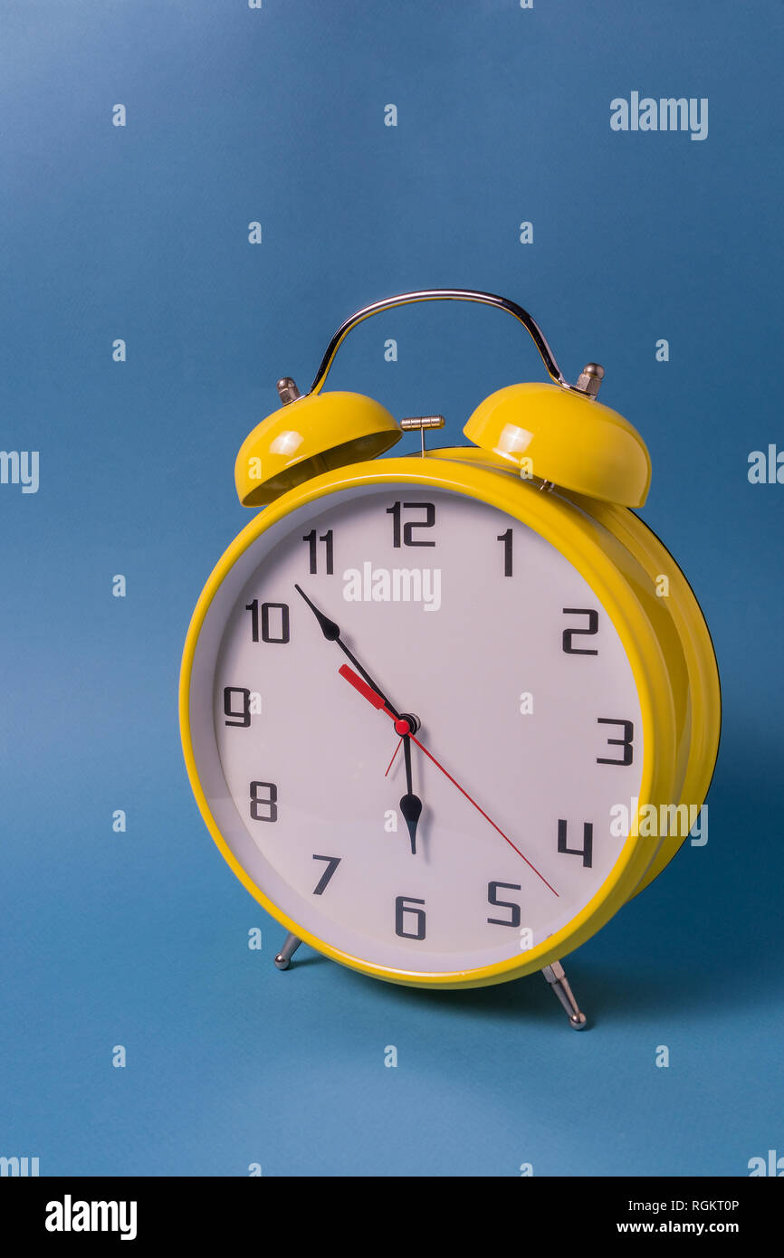 Reloj de alarma amarilla con siete minutos de six o'clock sobre fondo azul  Fotografía de stock - Alamy