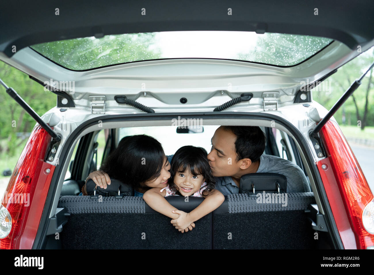 Feliz niña en un coche porque la madre y el padre amándola con besos Foto de stock