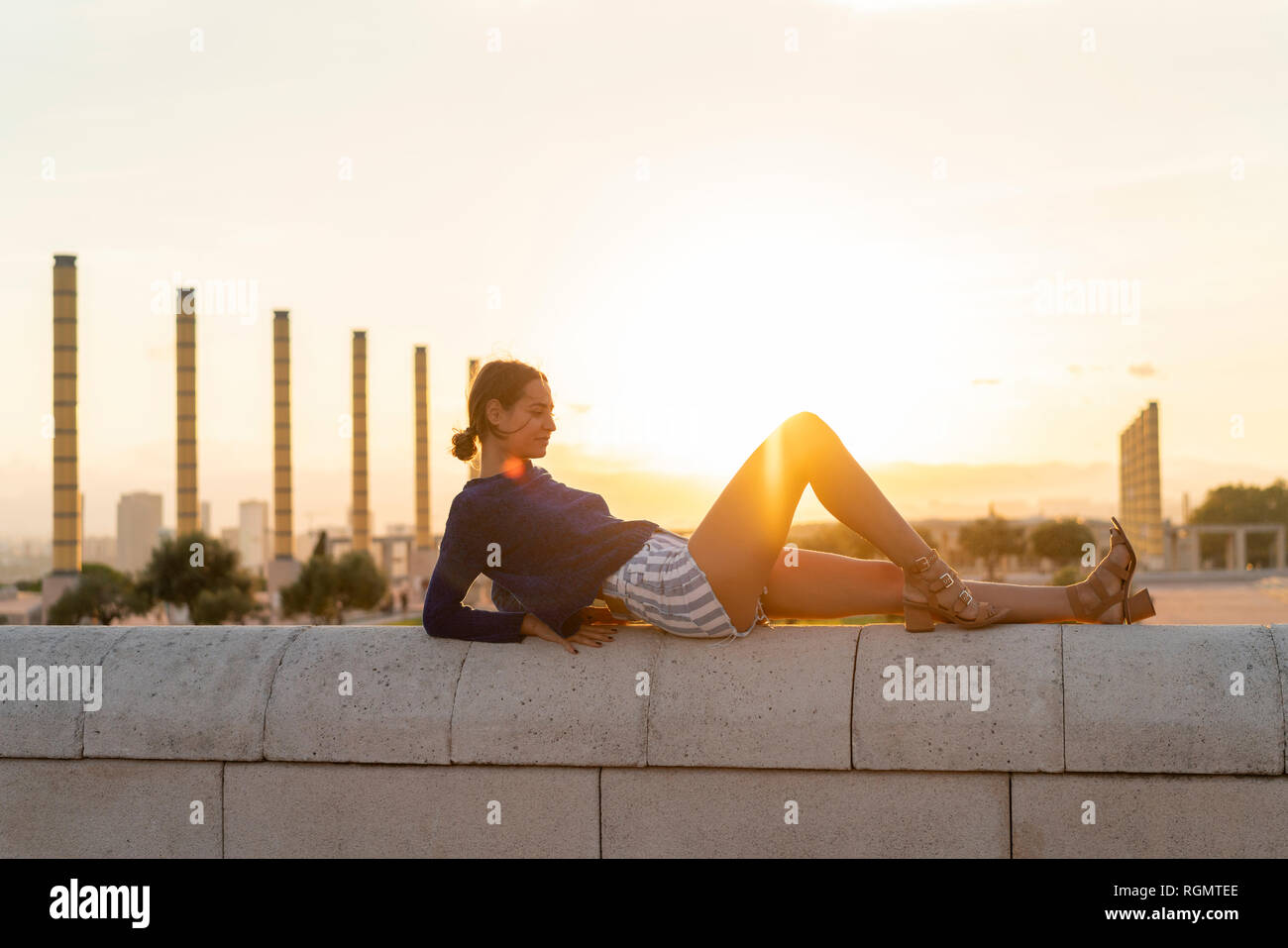 España, Barcelona, Montjuic, joven mujer acostada sobre una pared al atardecer Foto de stock