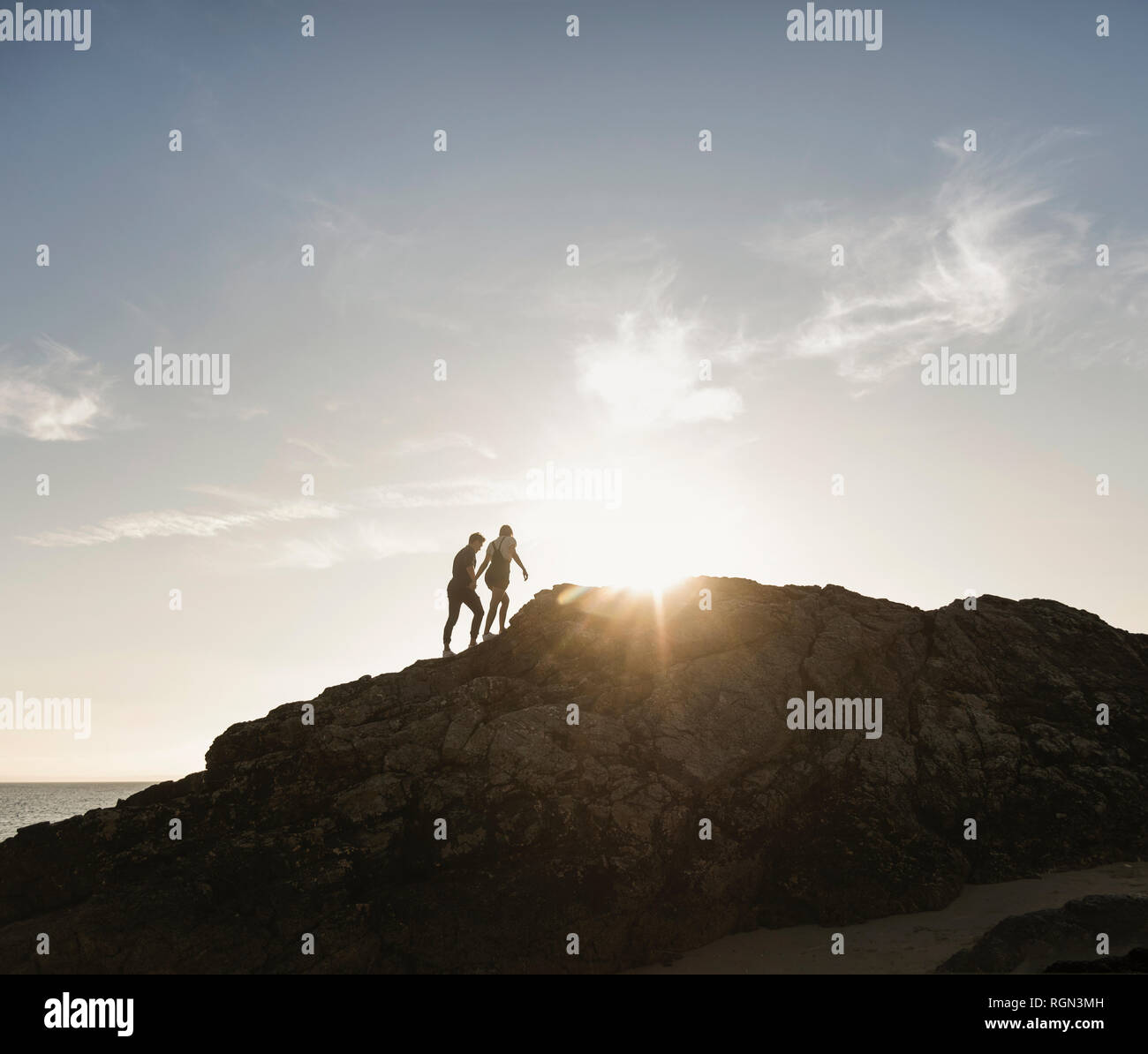 Francia, Bretaña, joven pareja de escalada en roca en la playa en el atardecer. Foto de stock