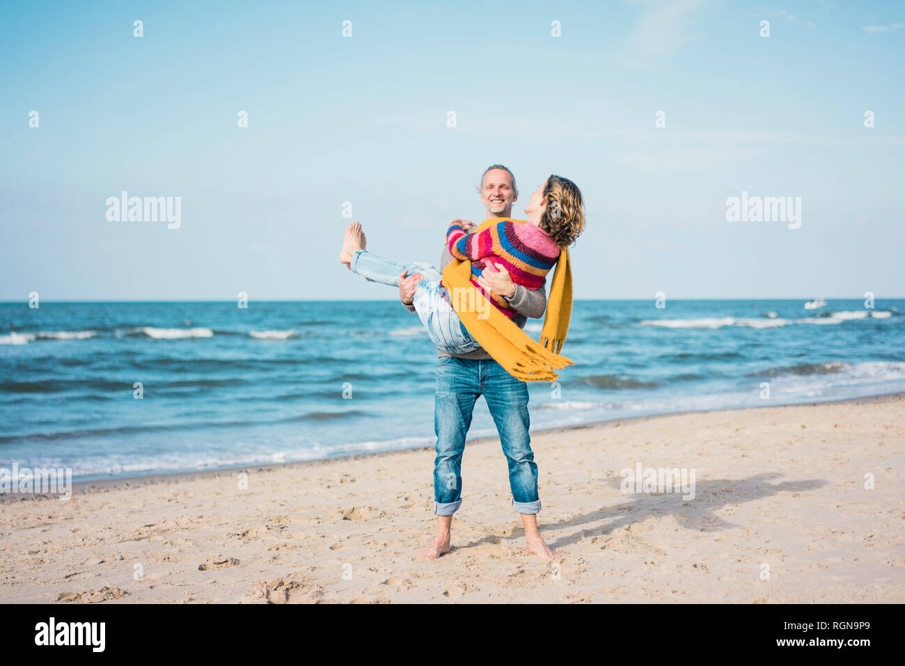 Feliz el hombre lleva en sus brazos a su esposa en la playa Foto de stock