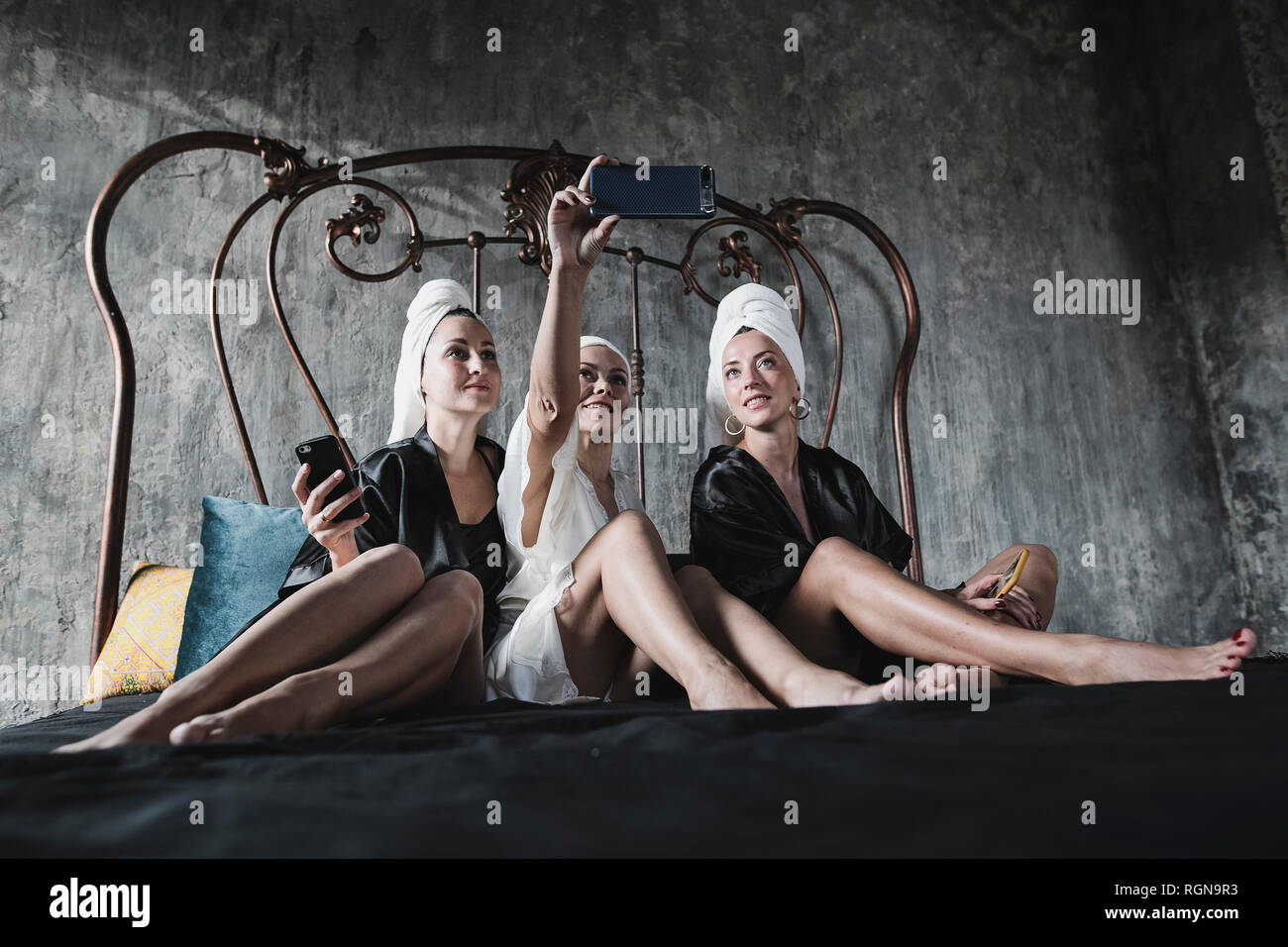 Tres mujeres con toallas alrededor de su cabeza en la cama tomando un selfie Foto de stock