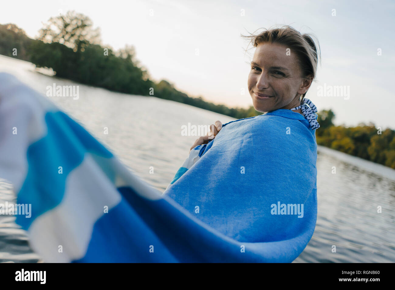 Retrato de mujer sonriente envuelta en una toalla en un lago Foto de stock