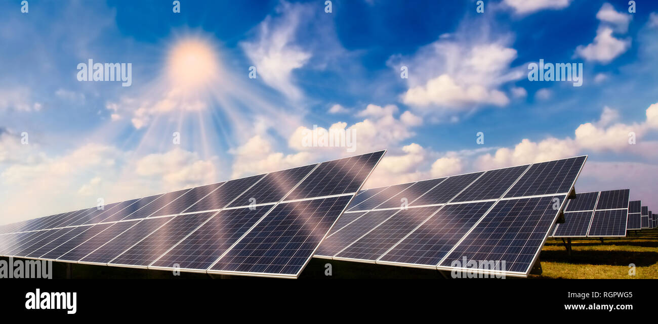 Sistema con módulos solares fotovoltaicos y sol brillante contra un cielo azul Foto de stock