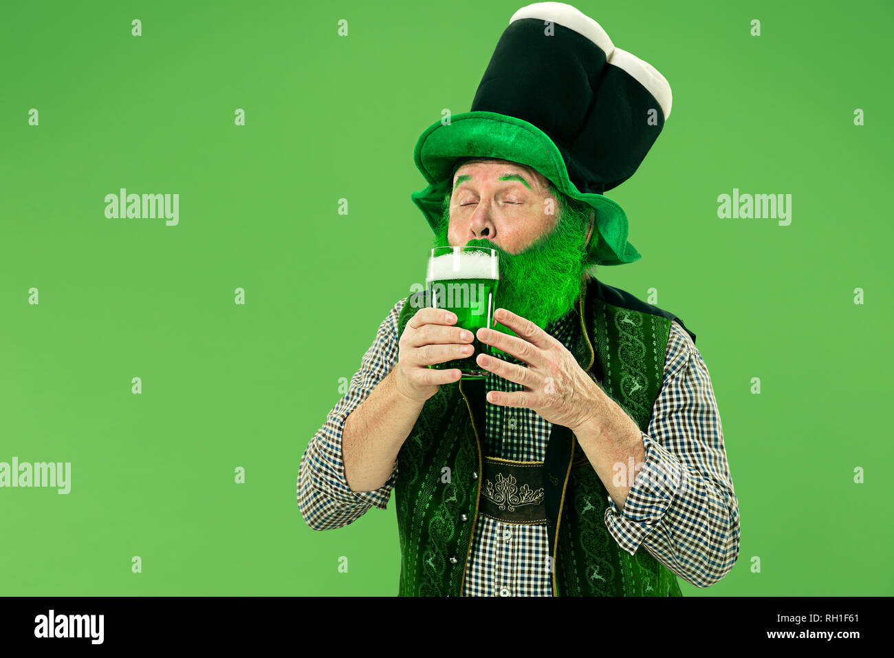 Un sonriente feliz senior hombre en un sombrero de duende con cerveza verde en el studio. Celebra el Día de San Patricio. La celebración, festiva, cerveza, vacaciones, alcohol, parte concepto Foto de stock