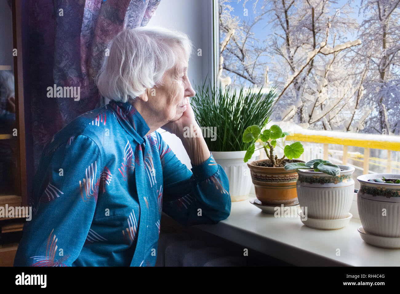 Old mujer solitaria sentado cerca de la ventana de su casa. Foto de stock