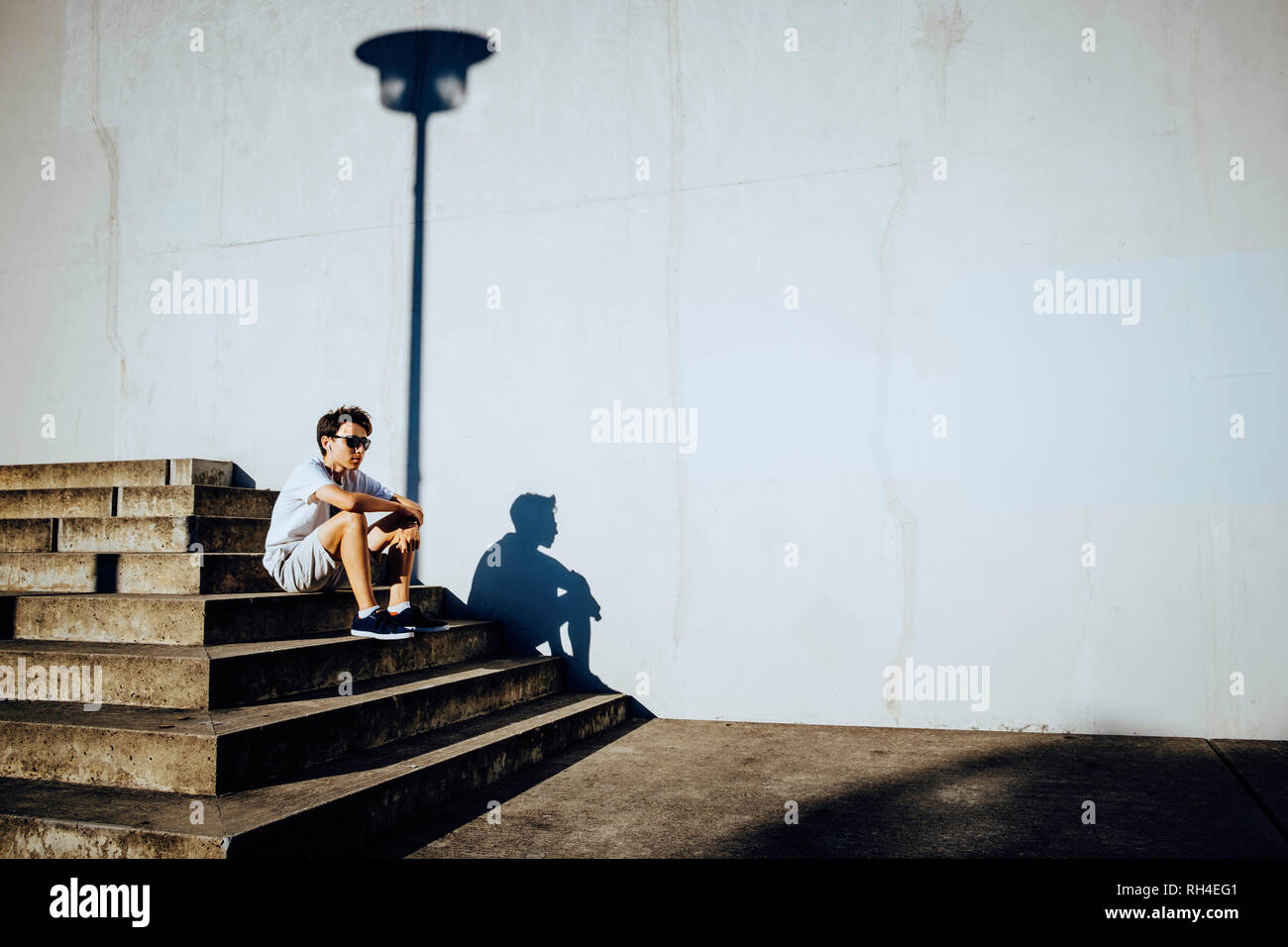 Macho joven corredor descansando sobre sunny pasos urbanos Foto de stock