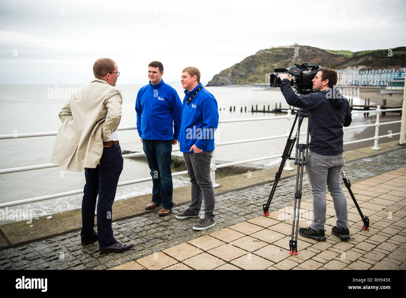 Los medios de difusión en el REINO UNIDO: un reportero de televisión de la BBC y el operador de cámara entrevistando a jóvenes en twoo Aberystwyth seafront, Gales, Reino Unido Foto de stock