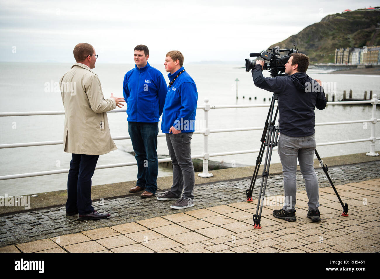 Los medios de difusión en el REINO UNIDO: un reportero de televisión de la BBC y el operador de cámara entrevistando a jóvenes en twoo Aberystwyth seafront, Gales, Reino Unido Foto de stock
