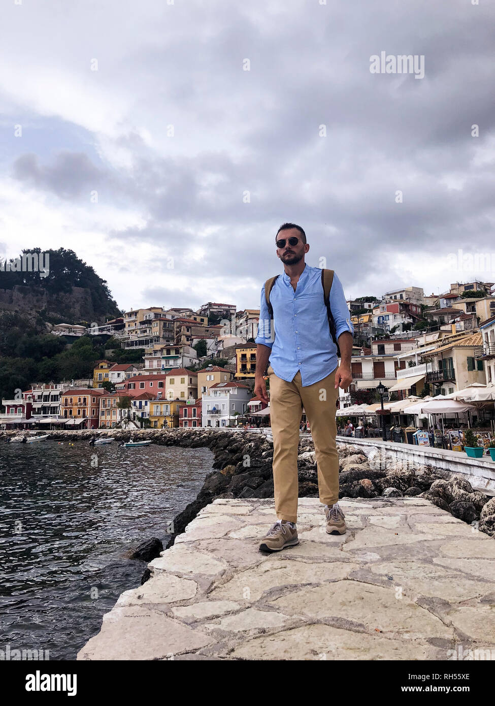 Retrato de un joven con pantalón marrón, camisa azul, gafas de sol y una  mochila marrón en Parga costa de Grecia Fotografía de stock - Alamy