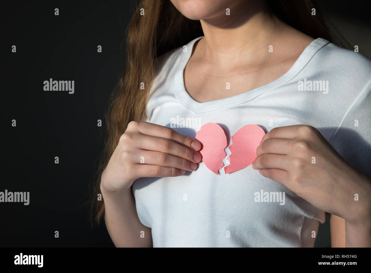Mujer en camisa blanca sujetando el papel roto corazón en el pecho Foto de stock