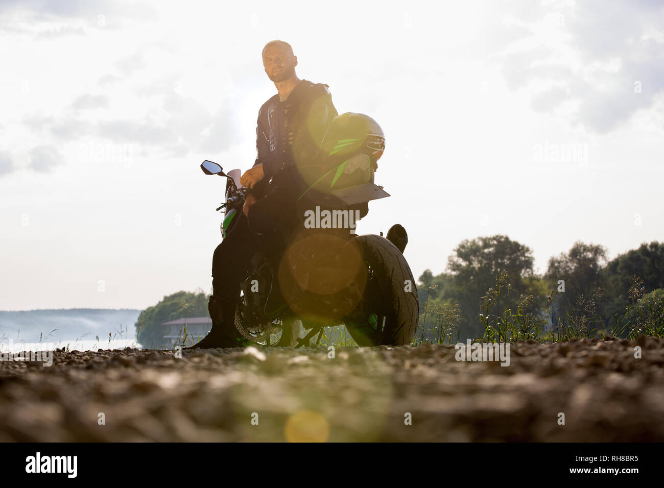 Biker hombre y la motocicleta con el río de fondo, Rider moto viaje en la calle, a la orilla del río, disfrutando de la libertad y un estilo de vida activo. Foto de stock