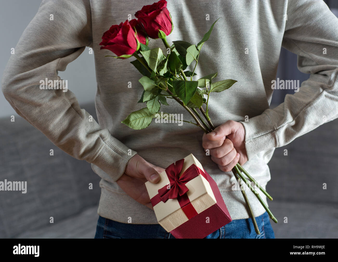 Hombre sujetando rosa roja flores y caja de regalo detrás de su 