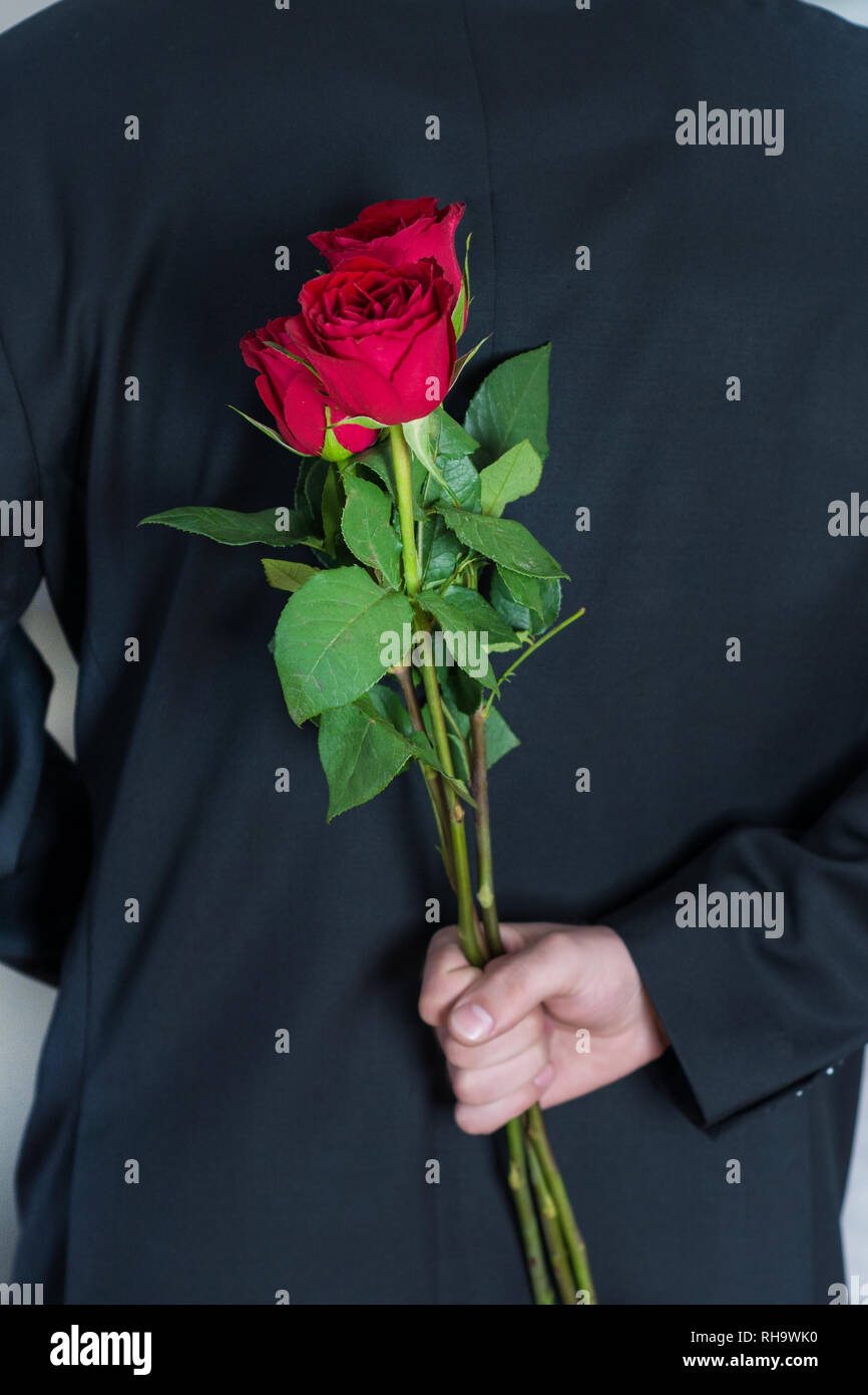 Hombre sujetando flores rosas rojas detrás de su espalda. Regalo 