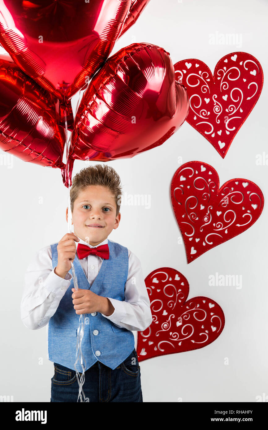 Día de San Valentín. Caballero guapo muchacho con chaleco azul, corbata roja, rosas rojas y cuchara globos rojos . San Valentín en niños. El amor y la amistad . Foto de stock