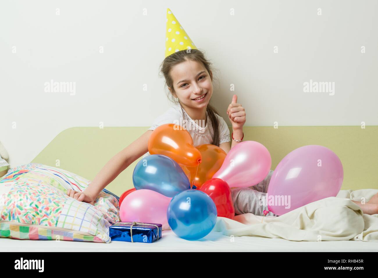 El cumpleaños de una adolescente es de 10-11 años. Una Niña de sombrero,  una fiesta con un regalo en la cama en una habitación infantil, globos de  fondo Fotografía de stock - Alamy