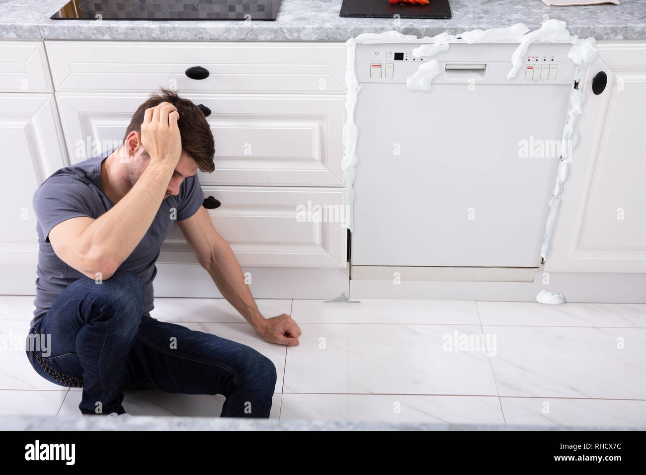 Malestar hombre sentado delante del lavavajillas dañado con la espuma que  sale del mismo Fotografía de stock - Alamy