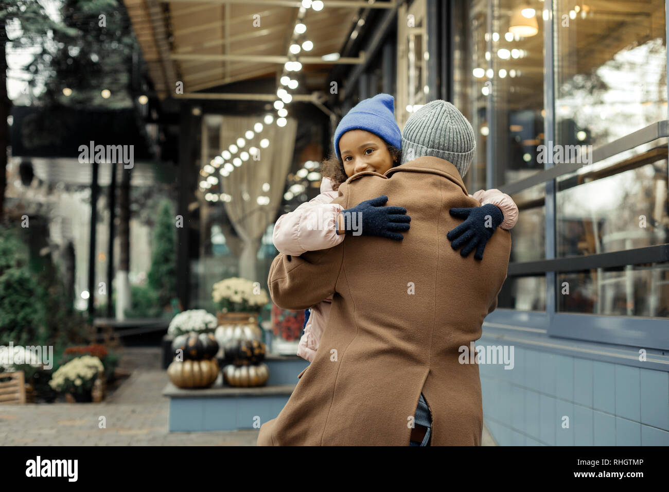Cute dark-eyed girl rizado vistiendo sombrero azul abrazando a su padre Foto de stock