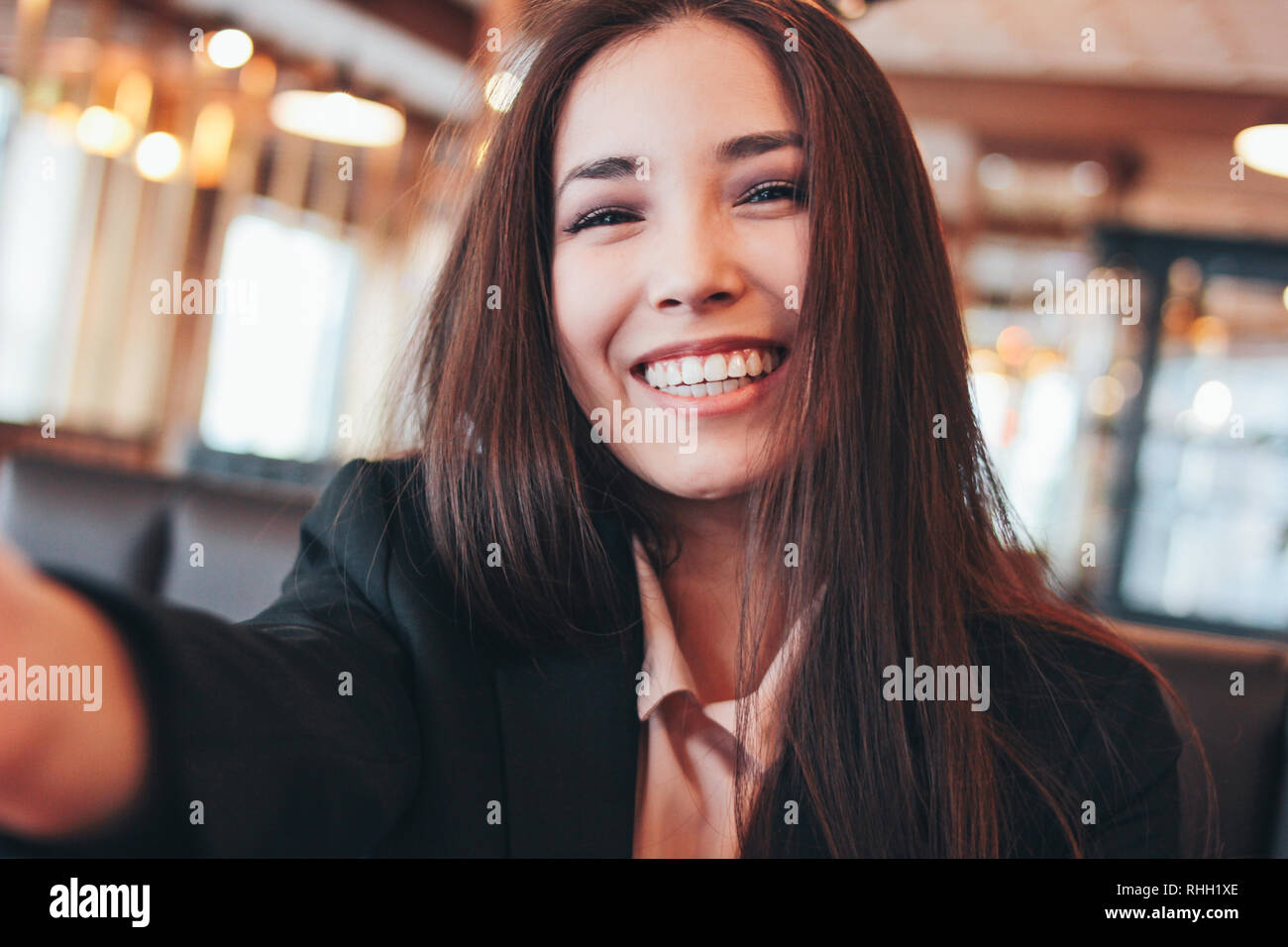 Hermosa morena encantadora chica asiática teniendo selfie sonriente en la cámara frontal en el cafe Foto de stock