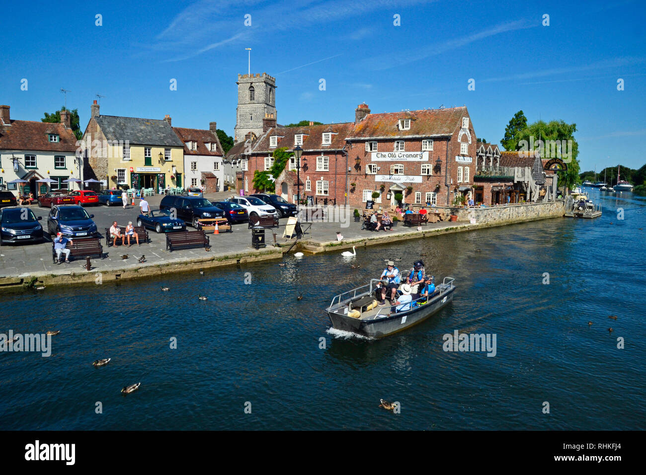 La gente en un pequeño bote a motor, viajando a lo largo del Río Frome. Los edificios en el muelle, Wareham en Dorset, Reino Unido, incluyen el antiguo pósito, cafetería y bar. Foto de stock