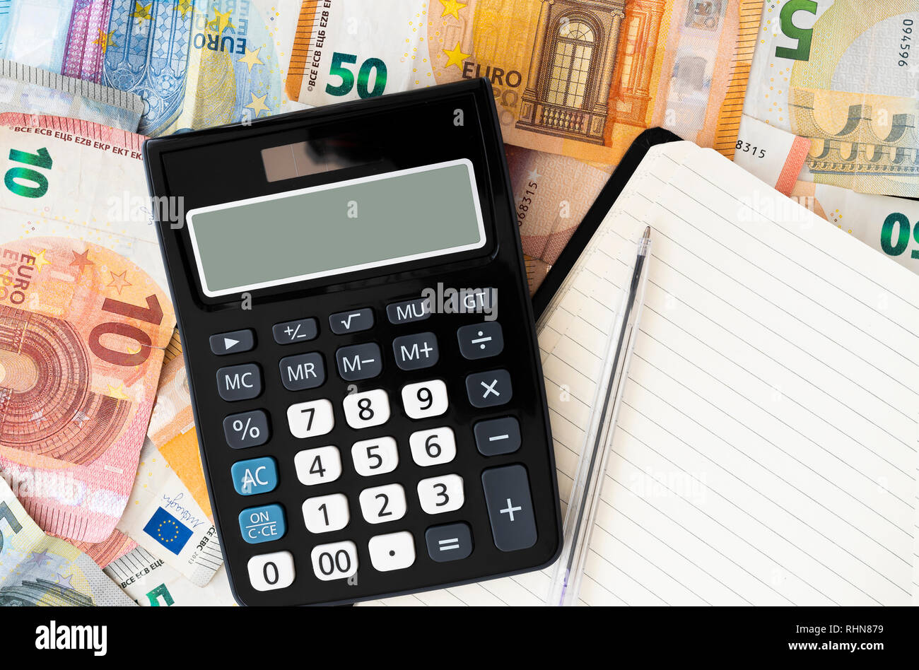Calculadora de bolsillo con billetes y monedas de euro en segundo plano. Foto de stock