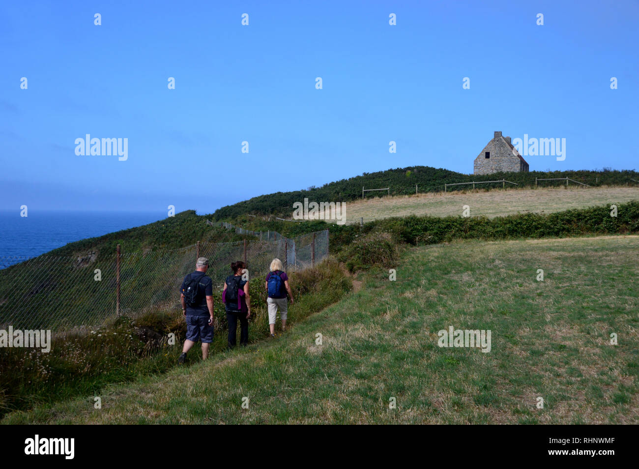 Tres excursionistas caminando hacia el monte del siglo XVIII Herault Watch House sobre la ruta costera en Guernsey, Islas del Canal.UK. Foto de stock