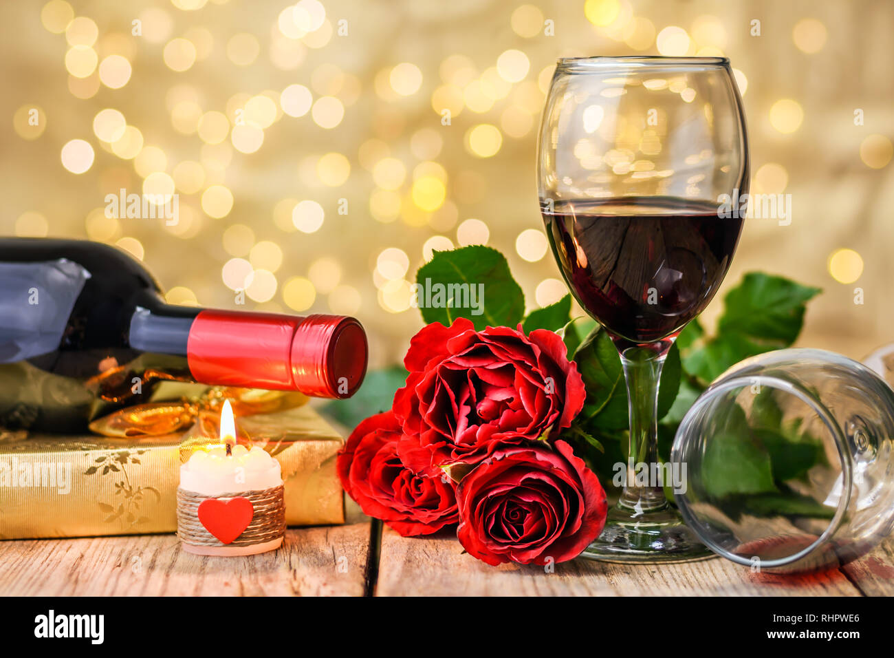 Concepto del Día de San Valentín. Dos copas de vino, rosas rojas, caja de  regalo, una botella de vino y velas encendidas sobre una tabla de madera  rústica en frente de un