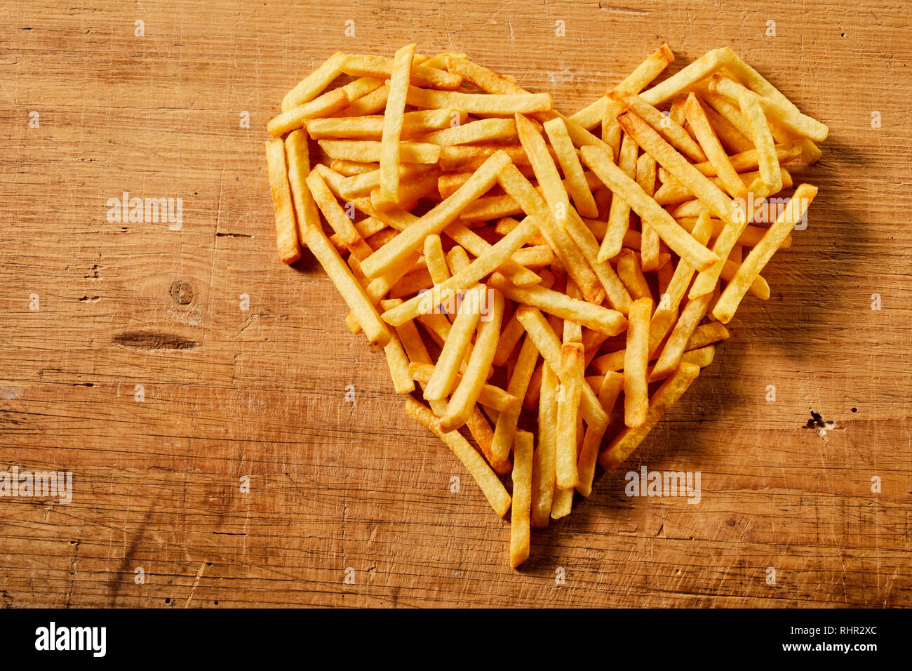 Vista desde arriba de una forma corazón hecho de sabrosas papas fritas servidas en una mesa de estilo rústico de madera como concepto de amor o comida rápida Foto de stock