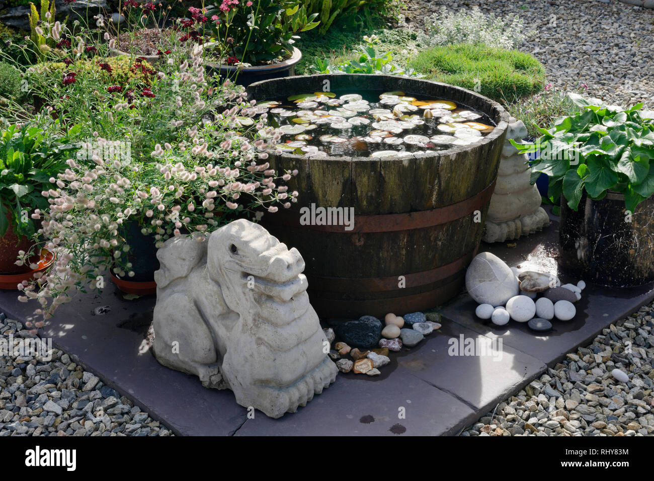 Jardín central un pequeño estanque de lirios creado en medio barril de whiskey, rodeado de plantas en macetas y casera dragon esculturas de hormigón. Foto de stock