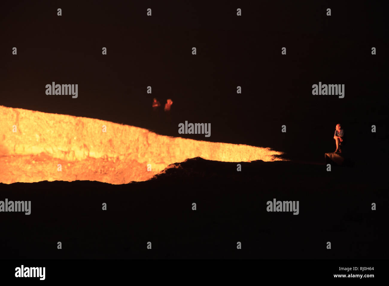 La gente que mira hacia abajo en el cráter Darvasa, también conocido como la Puerta al Infierno, el cráter de gas en llamas en Darvaza (Darvasa), Turkmenistán Foto de stock