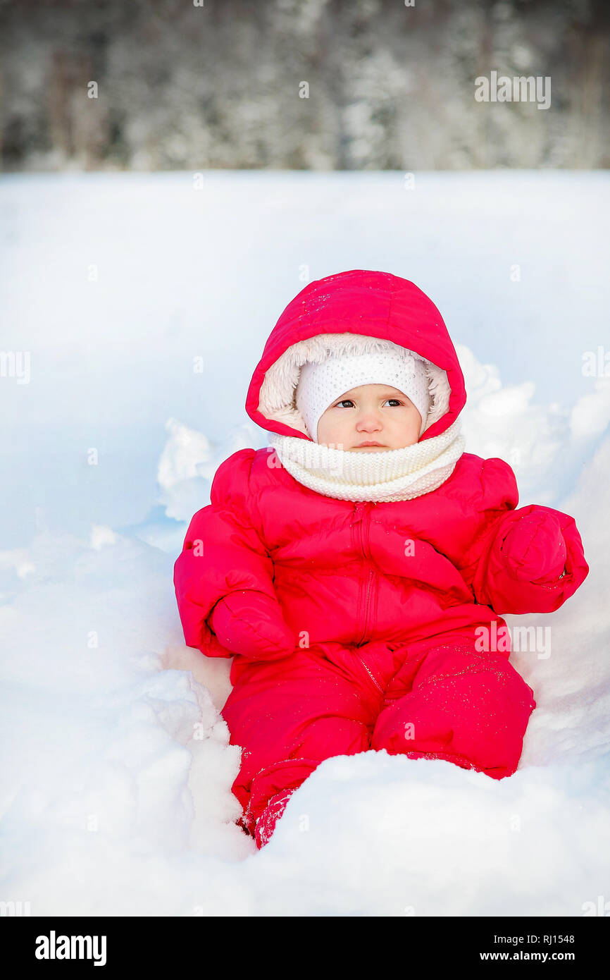 Los bebés pequeños en un mono rojo posando sentada en la nieve