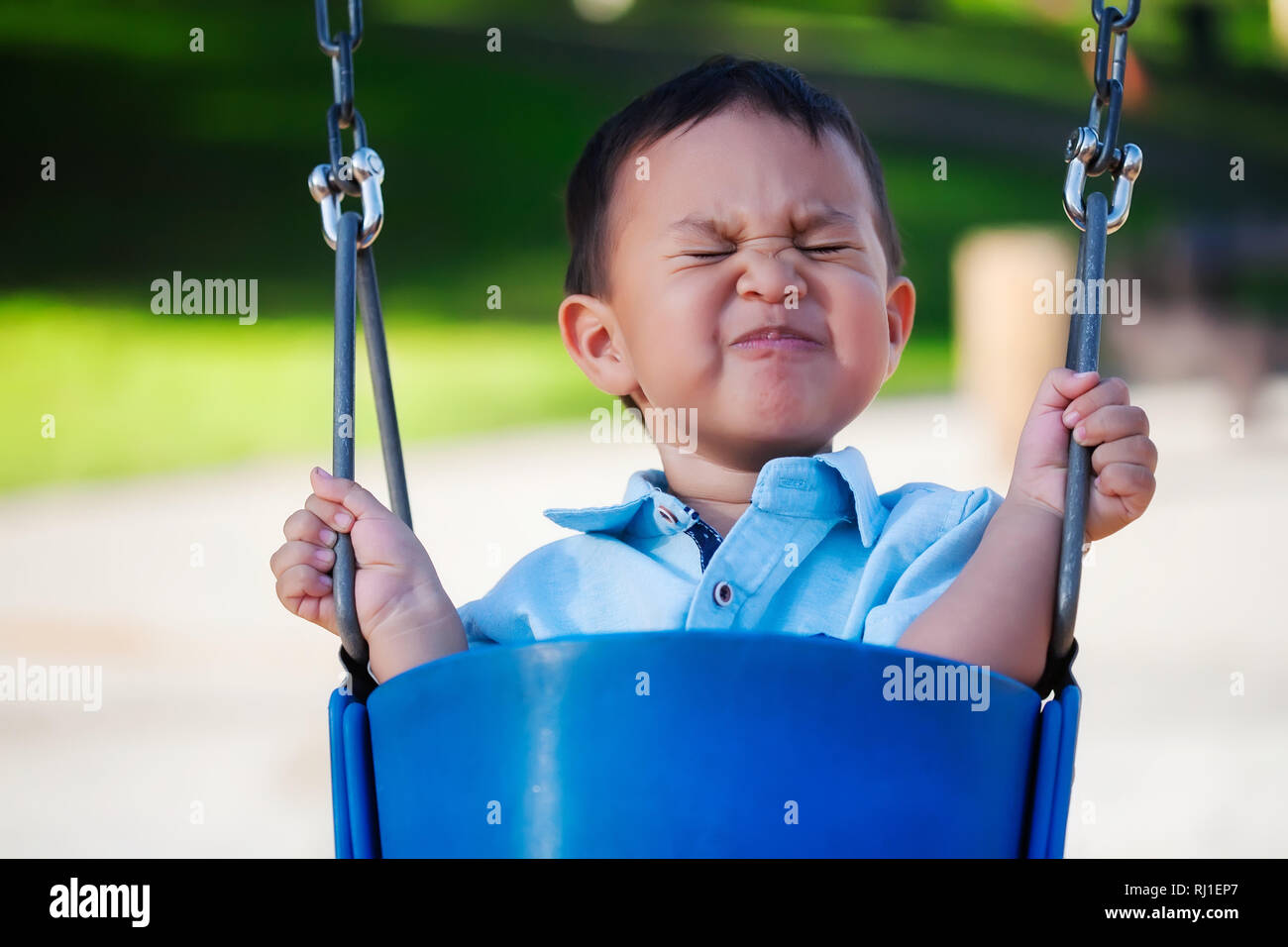 Little Boy montando un columpio con una expresión de miedo, sosteniendo con un férreo control porque él está asustado. Foto de stock