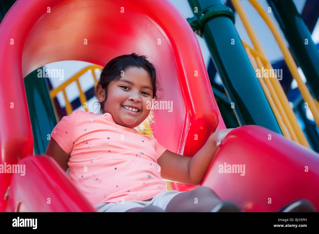 Una feliz y enérgica niña jugando en un parque infantil Rojo, acerca de la diapositiva a Diapositiva hacia abajo. Foto de stock