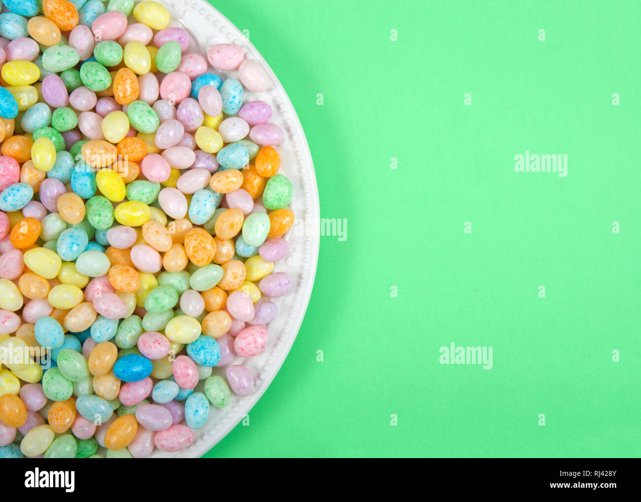 Muchos coloridos caramelos Jelly Beans en el plato de porcelana puesta sobre la superficie verde claro con espacio de copia. Populares dulces de pascua. Foto de stock