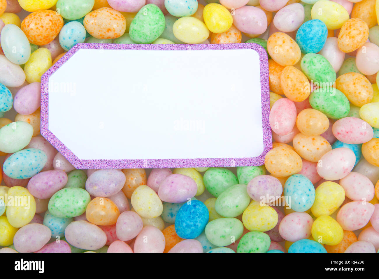 Muchos coloridos caramelos Jelly Beans en una superficie plana, tarjeta blanca con borde púrpura brillante espacio de copia. Tema de Pascua Foto de stock