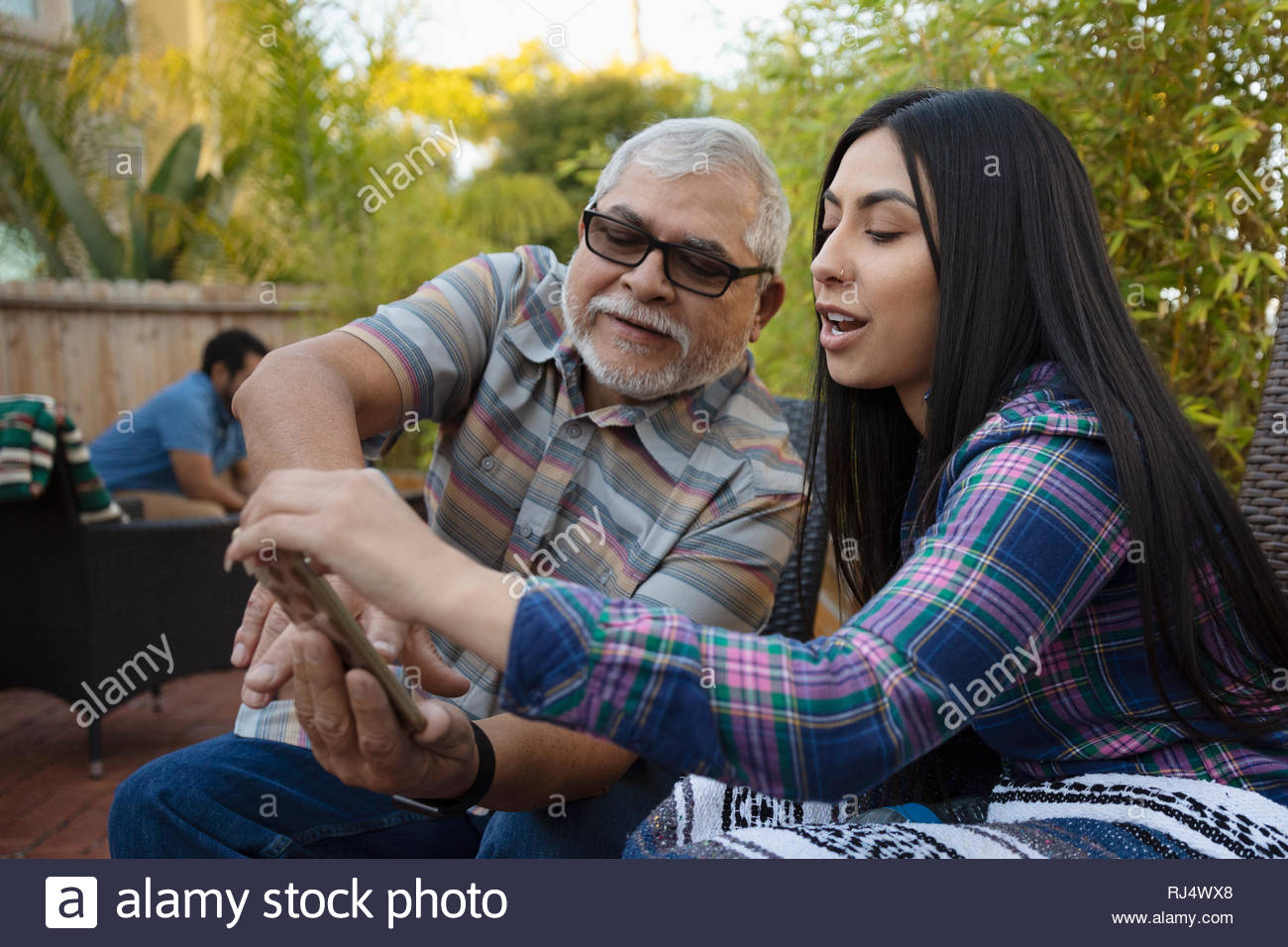 Abuelo y nieta Latinx utilizando smart phone en el patio Foto de stock