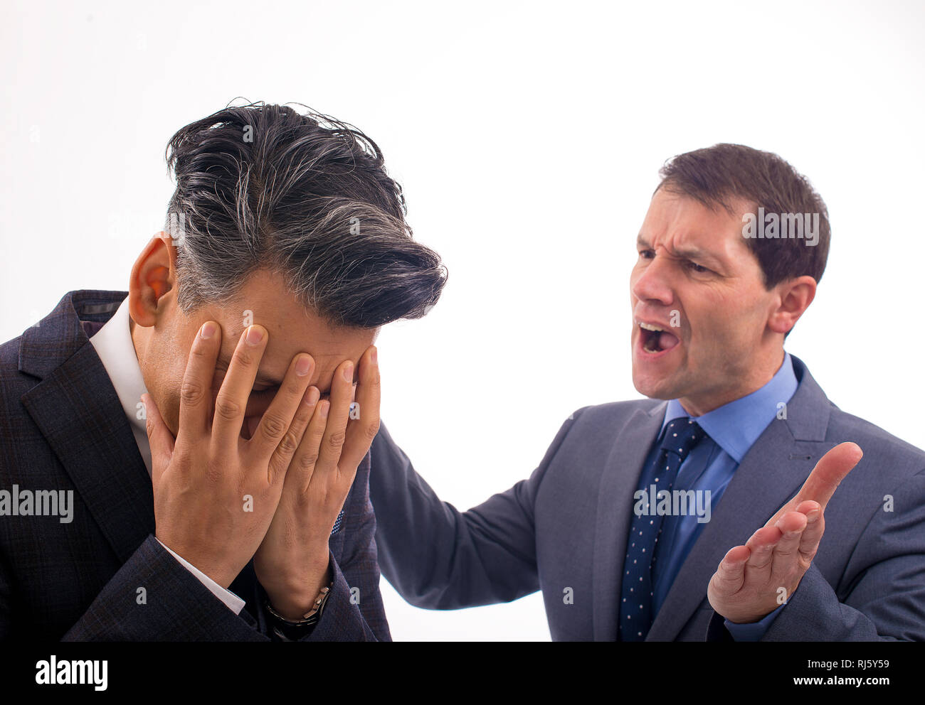Dos hombres de negocios que tienen un argumento contra un fondo blanco llano. Un hombre tiene su cabeza en sus manos y el otro le está gritando. Foto de stock