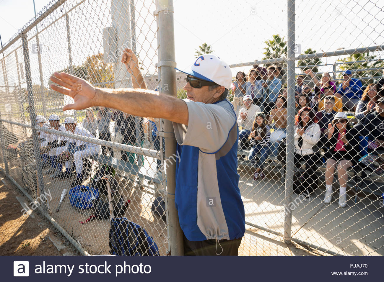 Entrenador de béisbol coaching desde detrás de la valla soleada Foto de stock