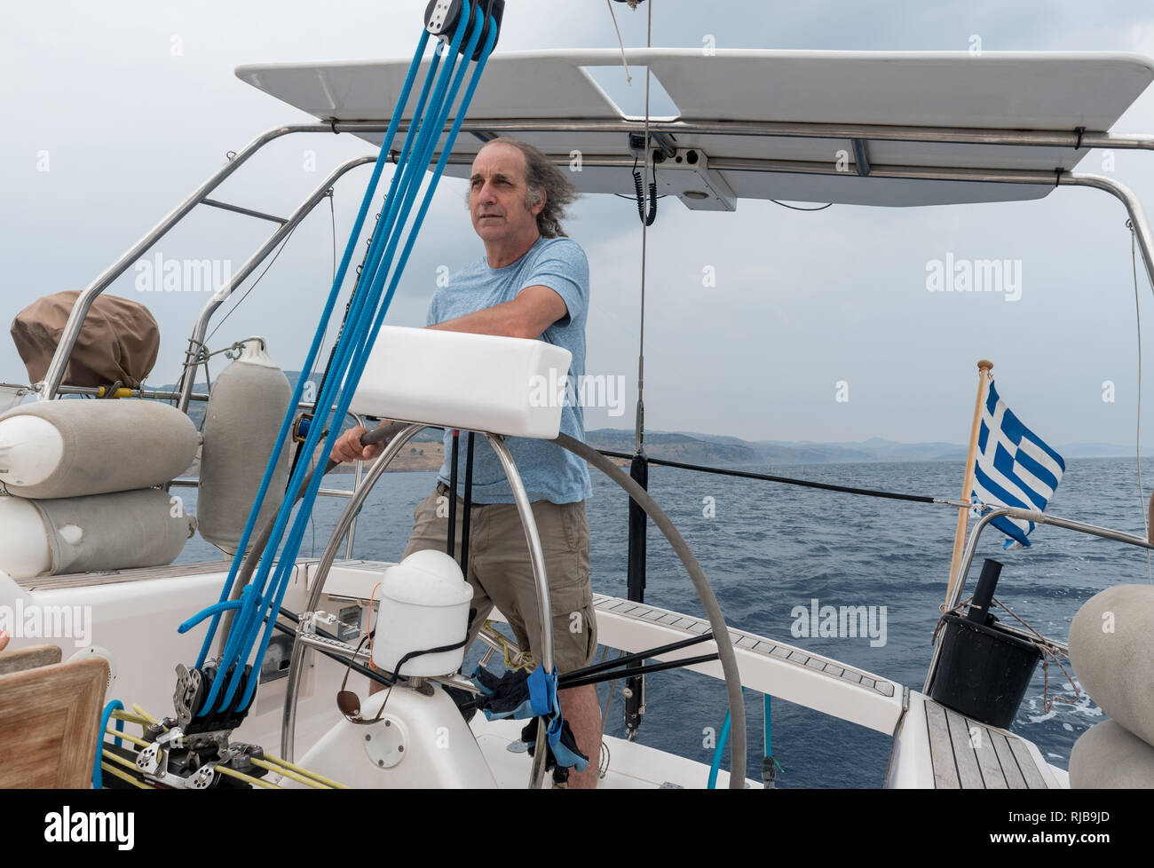 Senior Citizen al timón de un velero frente a la costa de Lesbos Foto de stock
