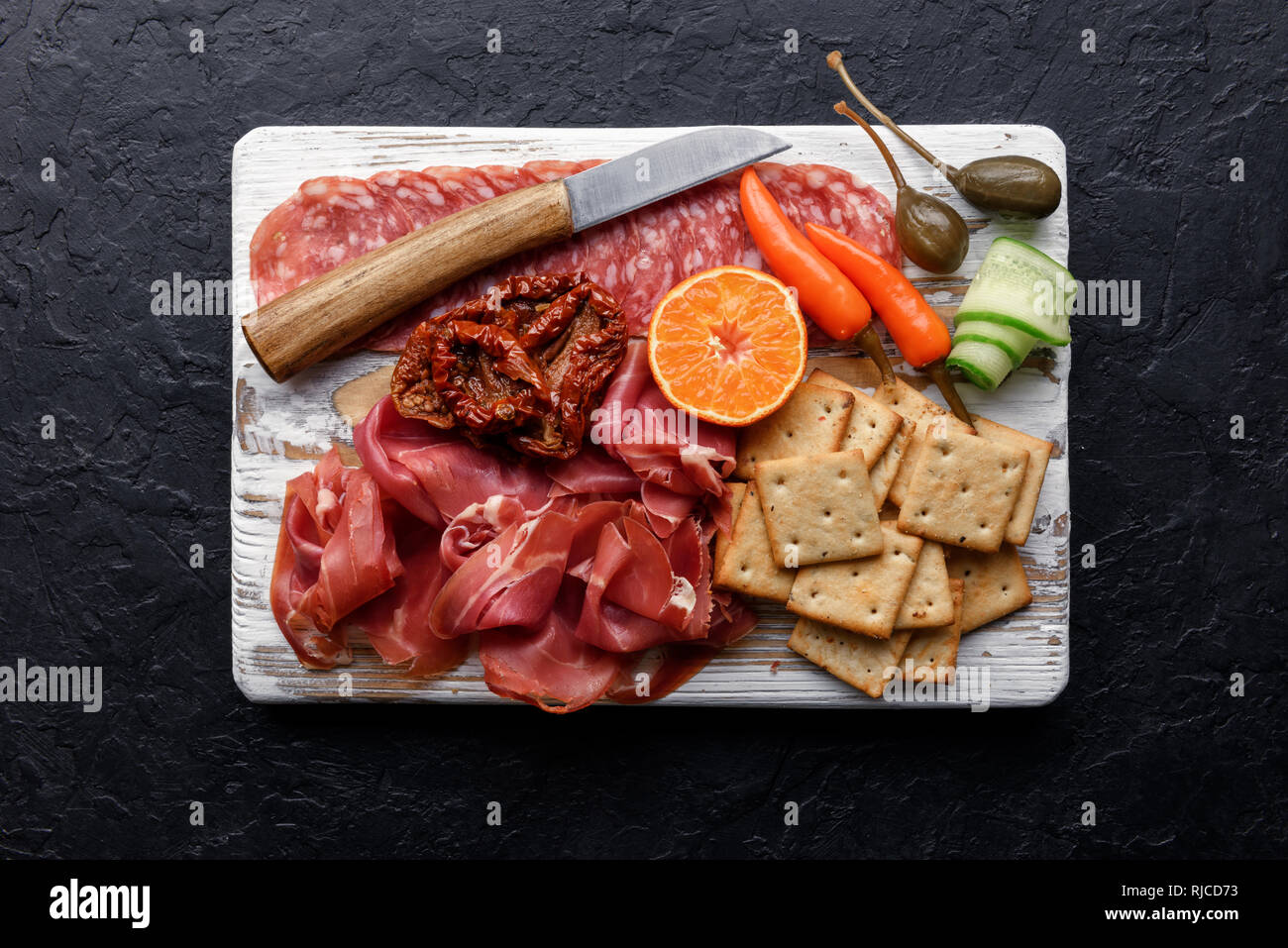 Antipasti italianos aperitivos. Alcaparras, jamón, salami y crackers más negro grunge tabla, vista desde arriba. Fotografía de alimentos Foto de stock