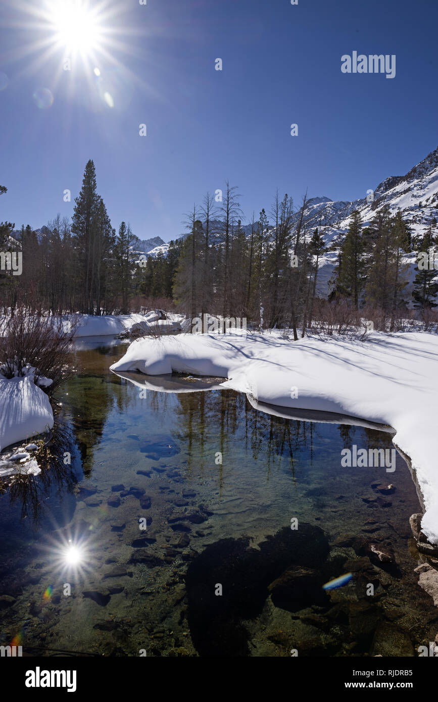 Oriente la horquilla del Obispo Creek en el invierno rodeado por la nieve con el sol en el cielo azul y se refleja en el agua Foto de stock