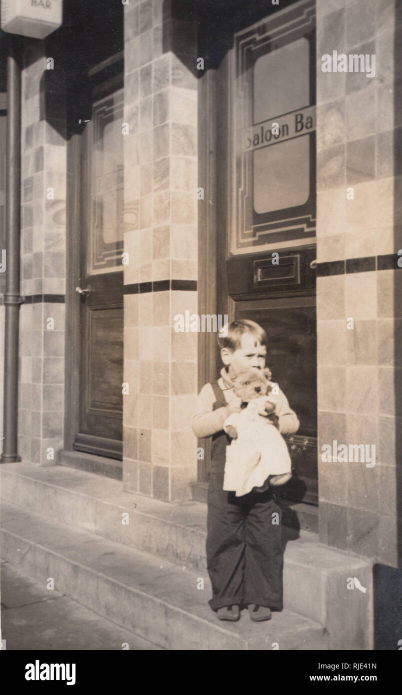 Vintage postales fotográficas de un joven niño sosteniendo un oso de peluche se situó en los escalones de una casa pública británica Foto de stock