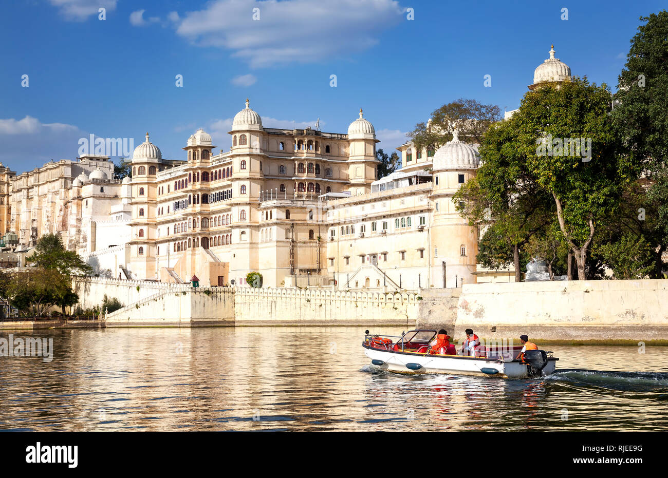 Barco con turistas en el lago Pichola con City Palace view en blue sky en Udaipur, Rajasthan, India Foto de stock