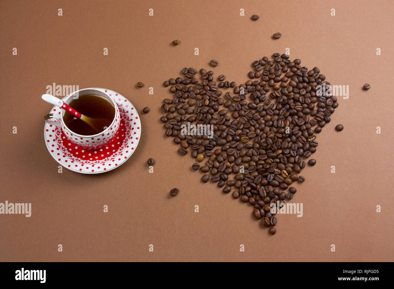 Vista superior de café negro polka dot cup y gran corazón hecho de granos de café sobre fondo marrón Foto de stock