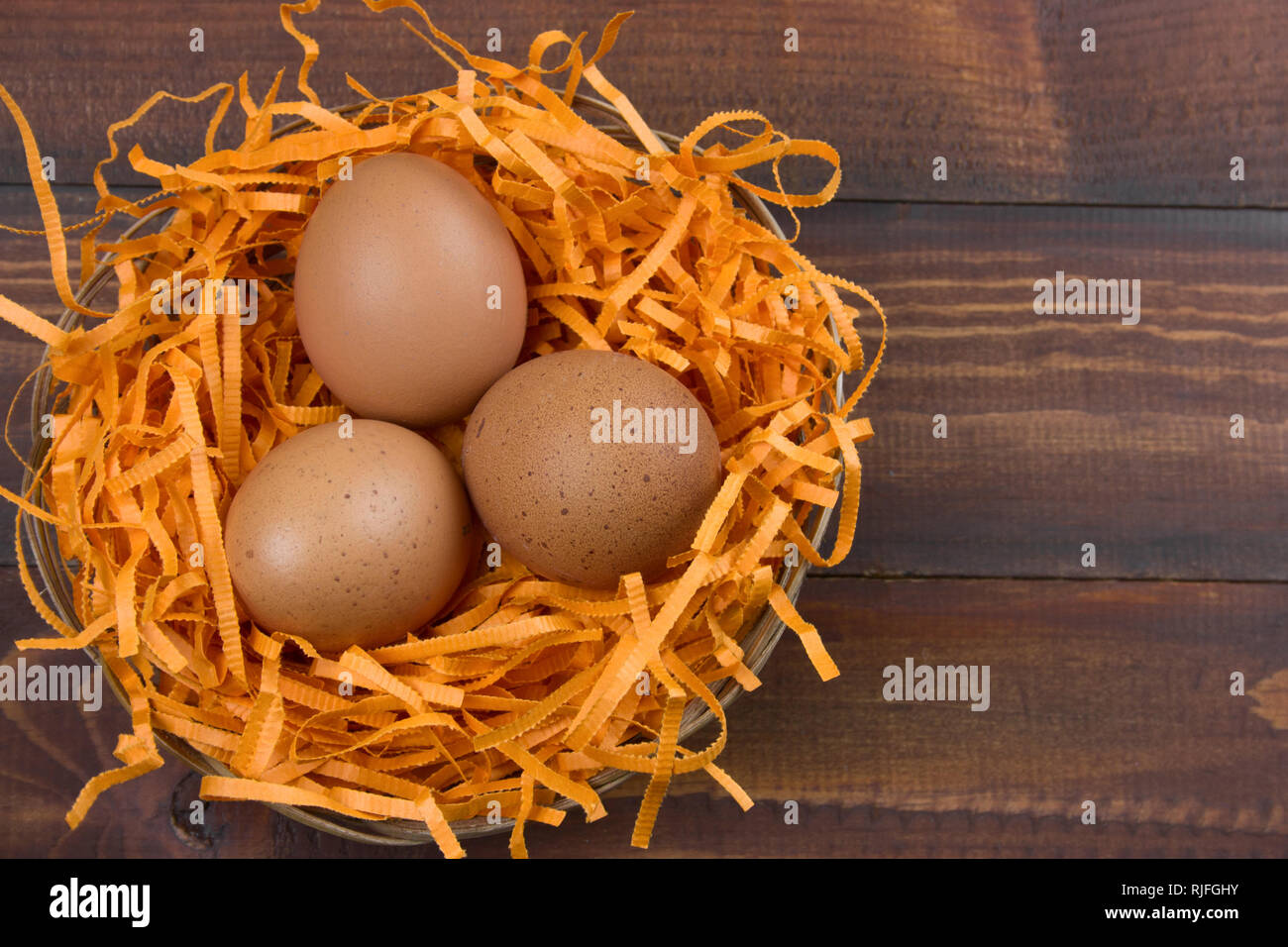 Vista superior marrón de huevos en un nido decorativo sobre un fondo de madera Foto de stock