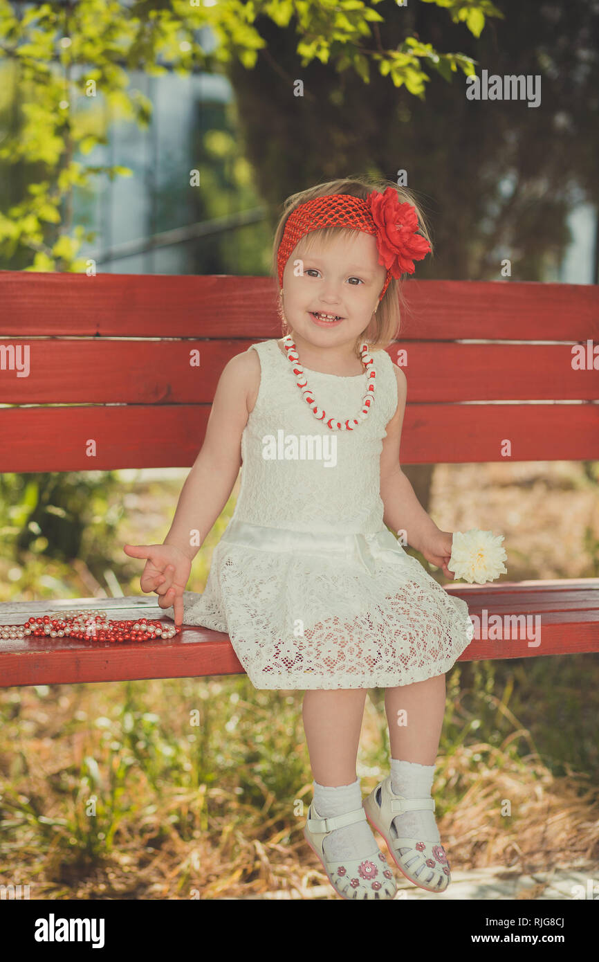 Retro elegante vestido bebé joven rubia posando en Central park garden vistiendo francés couturer blanco pañuelo rojo y adorno Fotografía de stock - Alamy