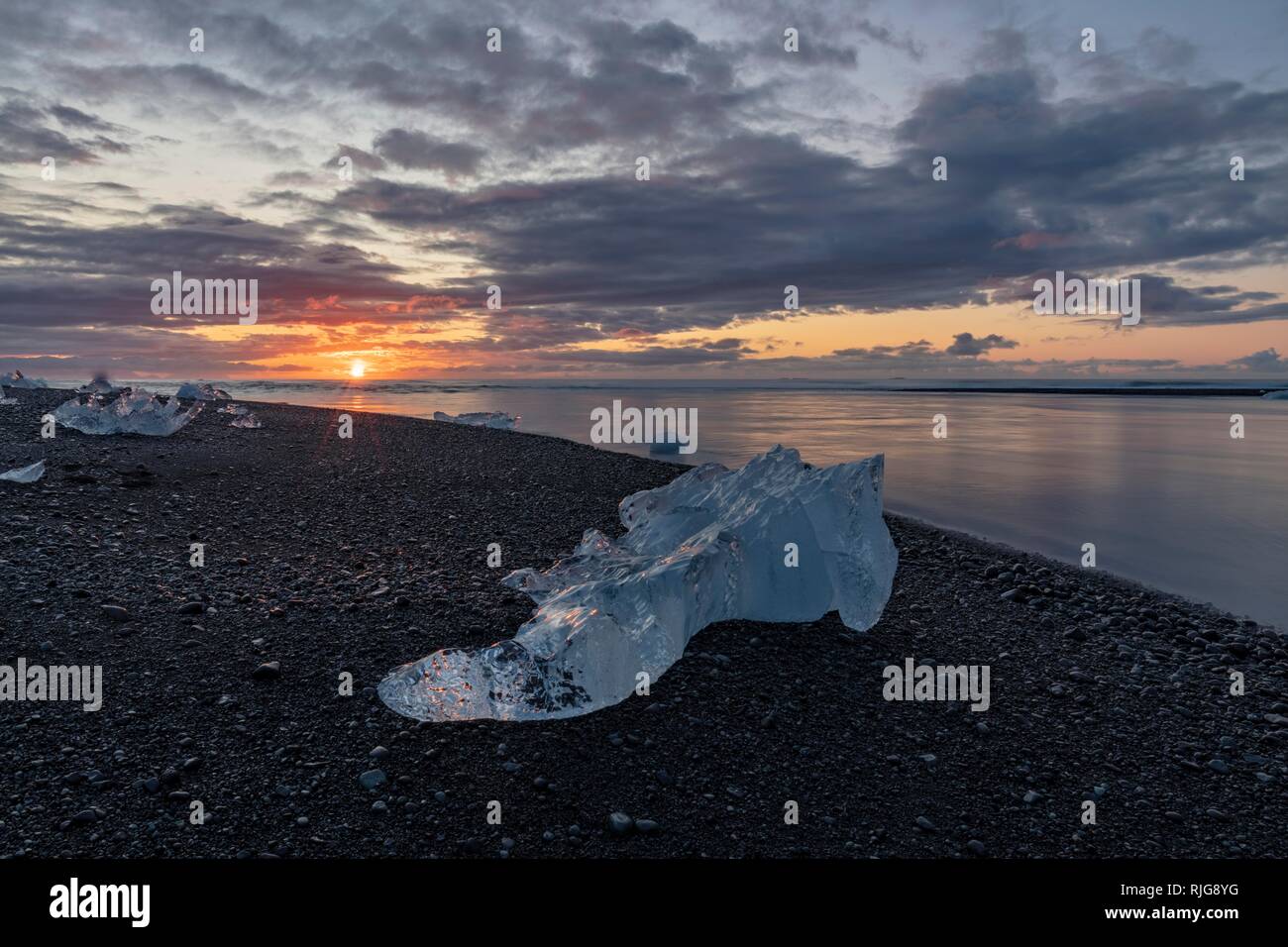 Témpano de hielo en la playa al amanecer de lava negra, laguna glaciar Jökulsárlón, Islandia Foto de stock