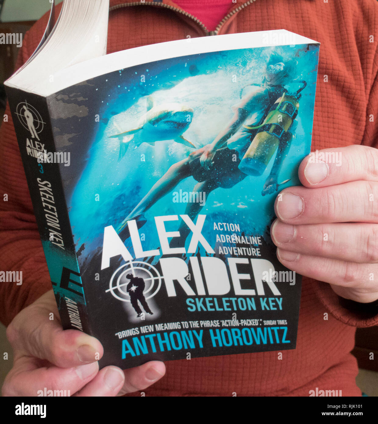 Persona leyendo caucásica Alex Rider Skeleton Key ficticia de libro de bolsillo por Anthony Horowitz Foto de stock