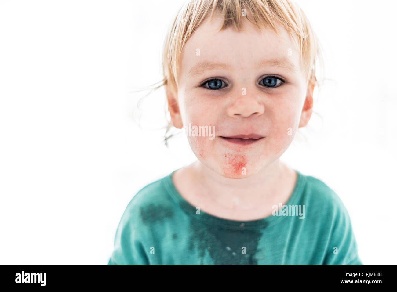 Un bonito retrato artístico de un joven muchacho sonriente con ojos azules que acaba de comer sandía. El niño está mirando directamente a la cámara. Foto de stock
