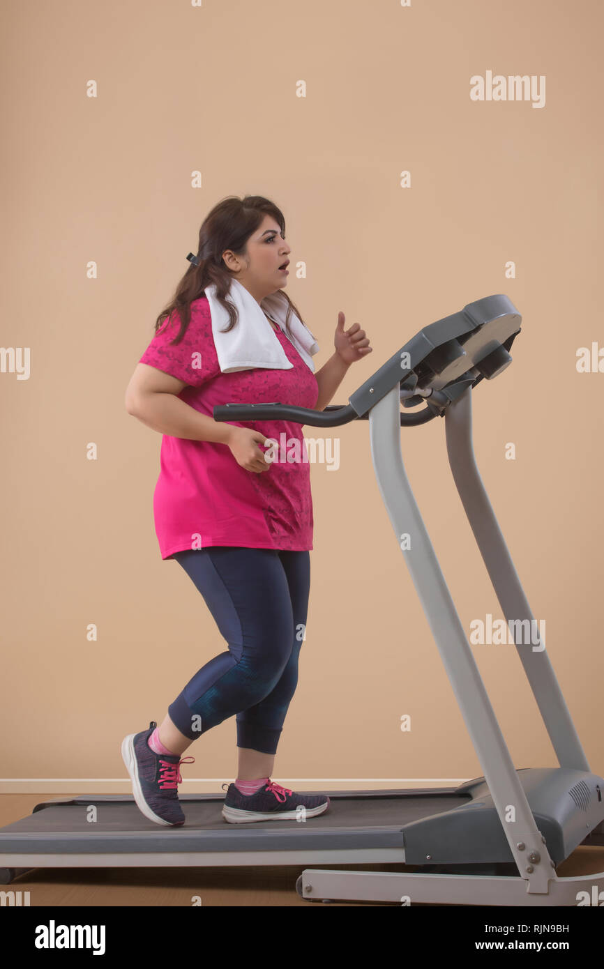 Chica deportiva en ropa deportiva roja corre en cinta de correr en el  gimnasio mujer entrena en la sala de fitness